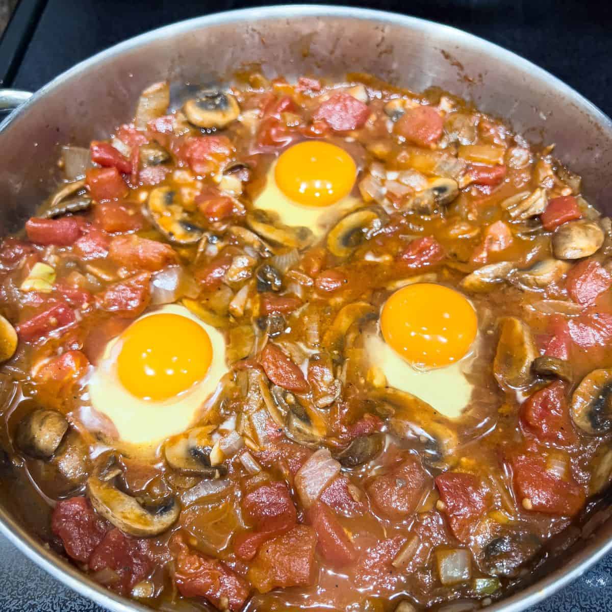 Adding eggs to finish up the mushroom shakshuka dish.
