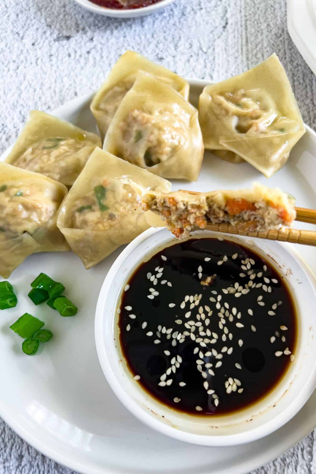 Taking a bite of vegan tofu dumplings with a dip.