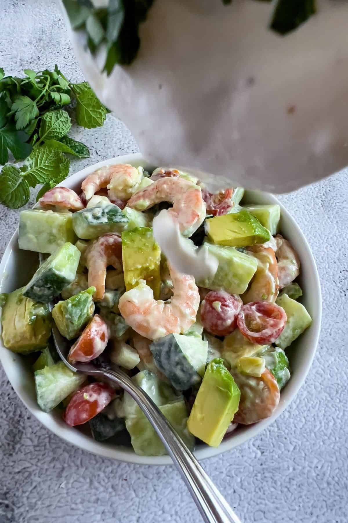 Pouring more salad dressing into a bowl of salad.
