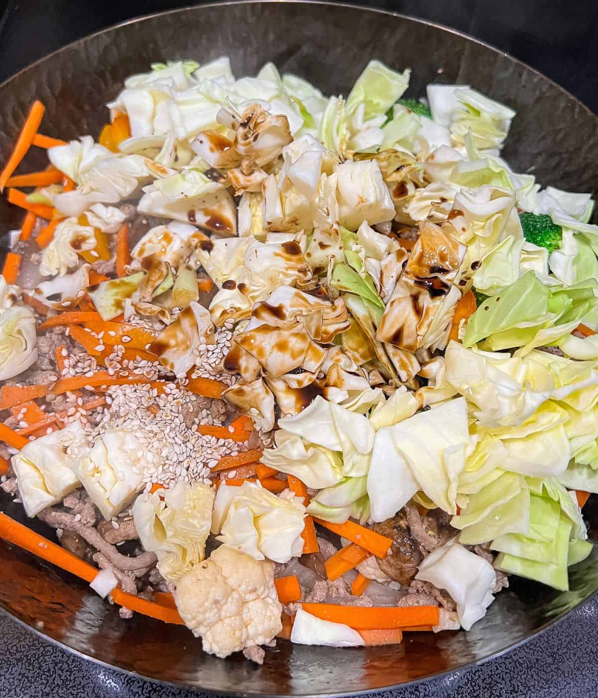 Adding cabbage, soy sauce, sesame oil and sesame seeds.