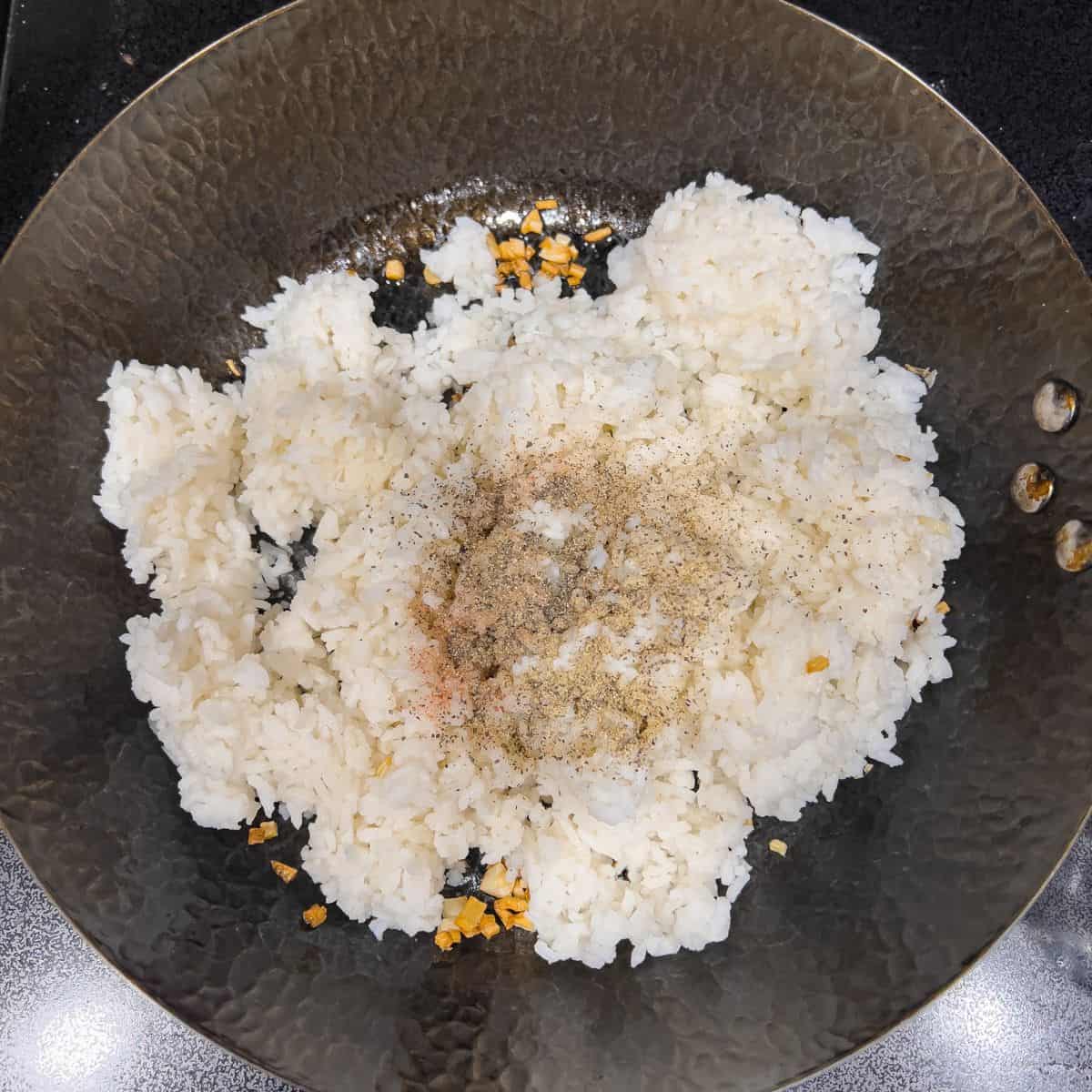 Adding rice, salt and pepper to make garlic fried rice dish.