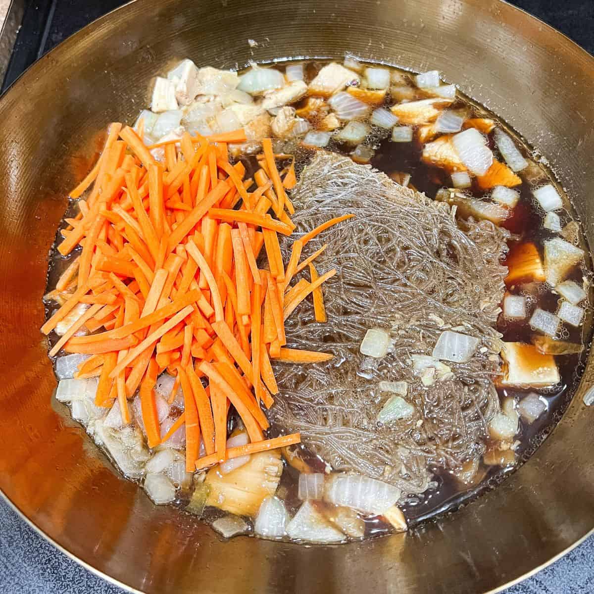 Adding carrots, shrimp stock, soy sauce and bihon noodles.