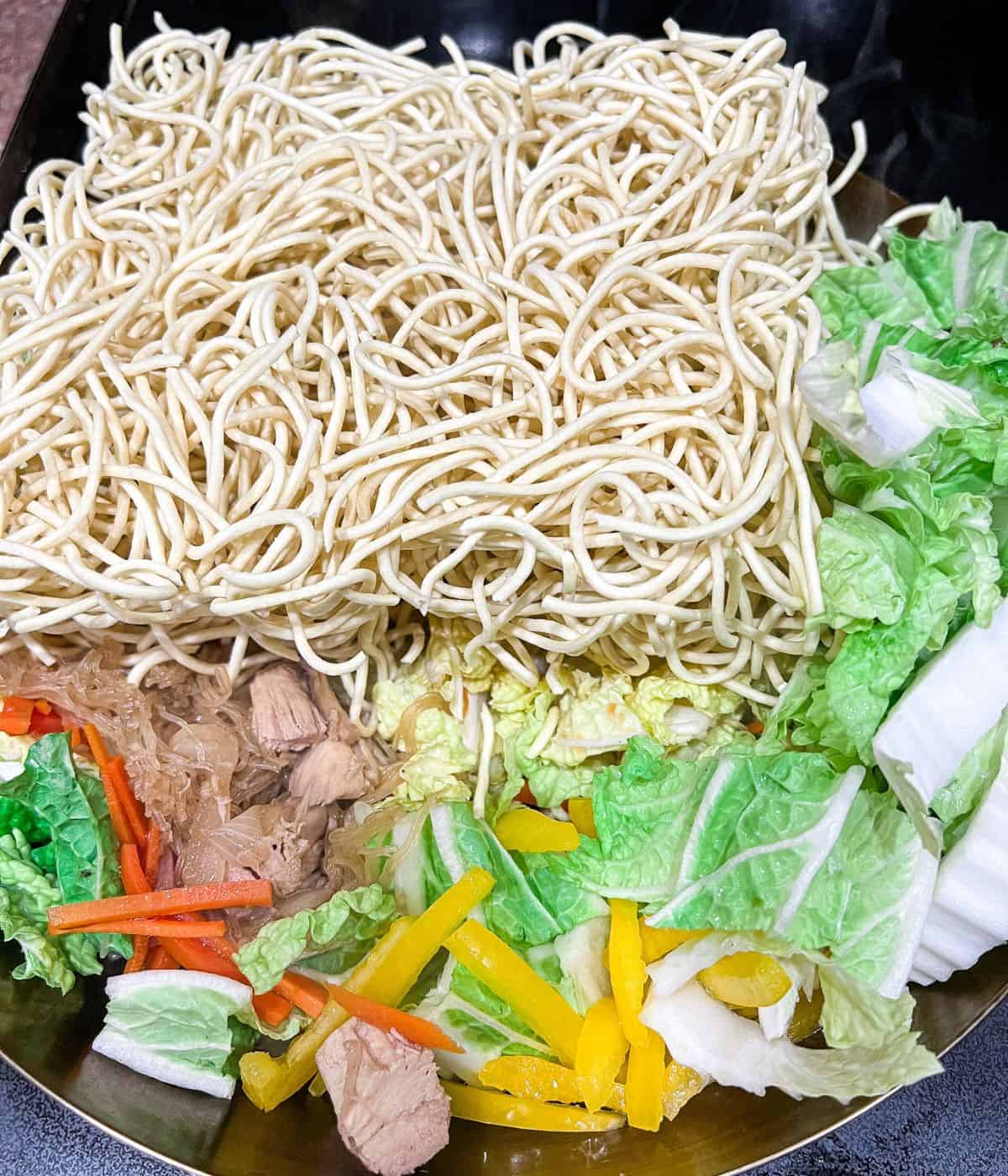 Cooking vegetables and egg noodles to make pancit canton and bihon.