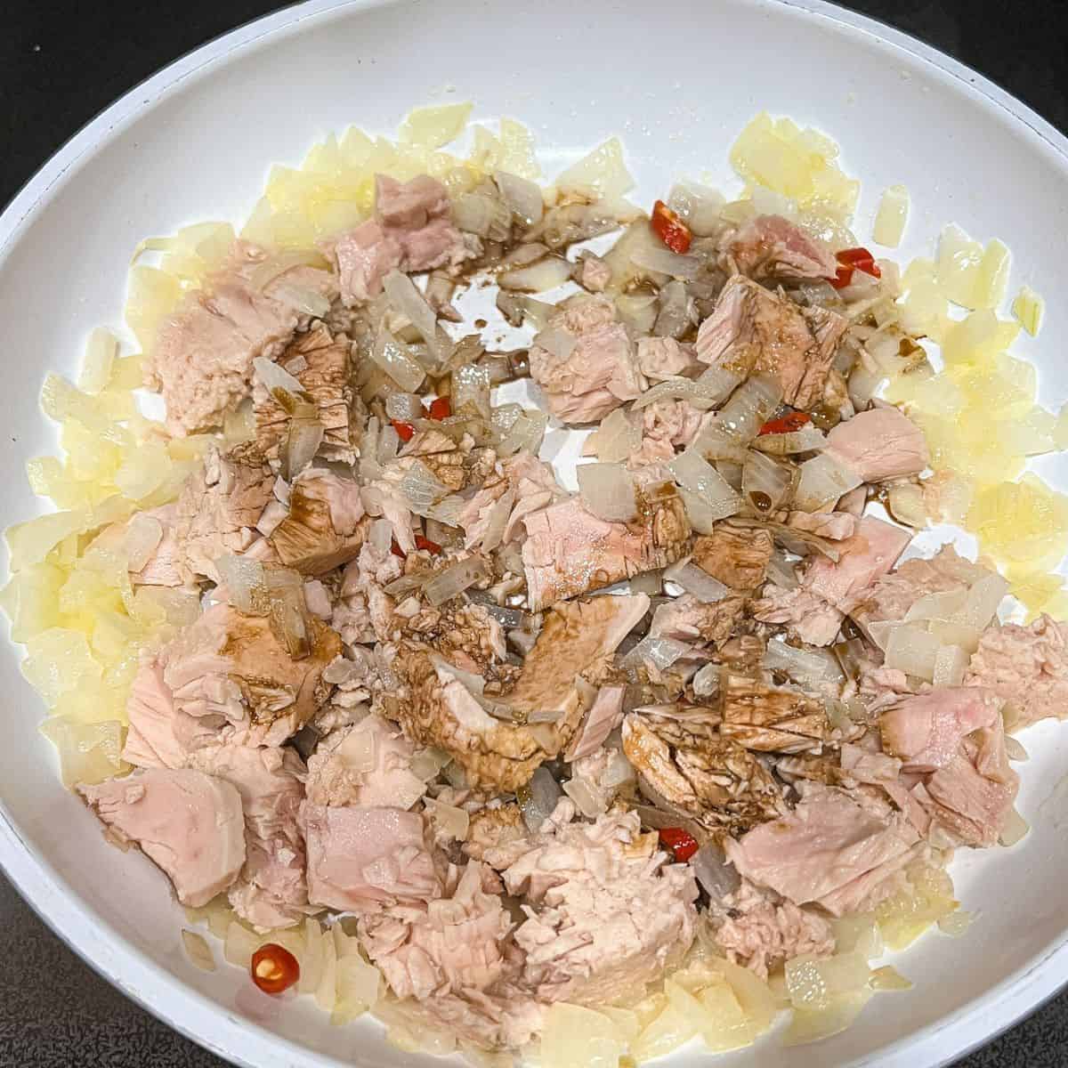Adding tuna, soy sauce, and red chili to the dish.