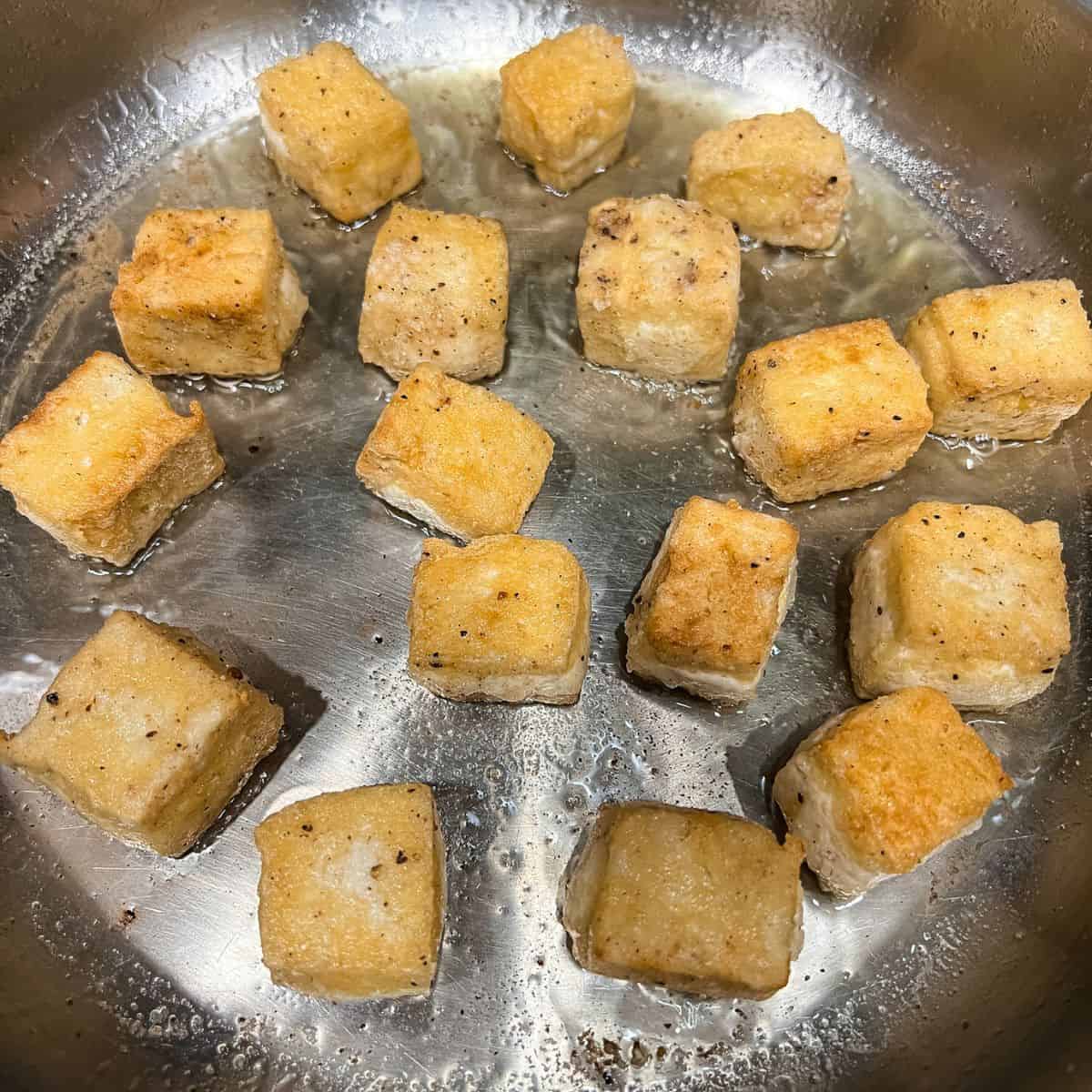 Frying tofu until crispy and golden brown.