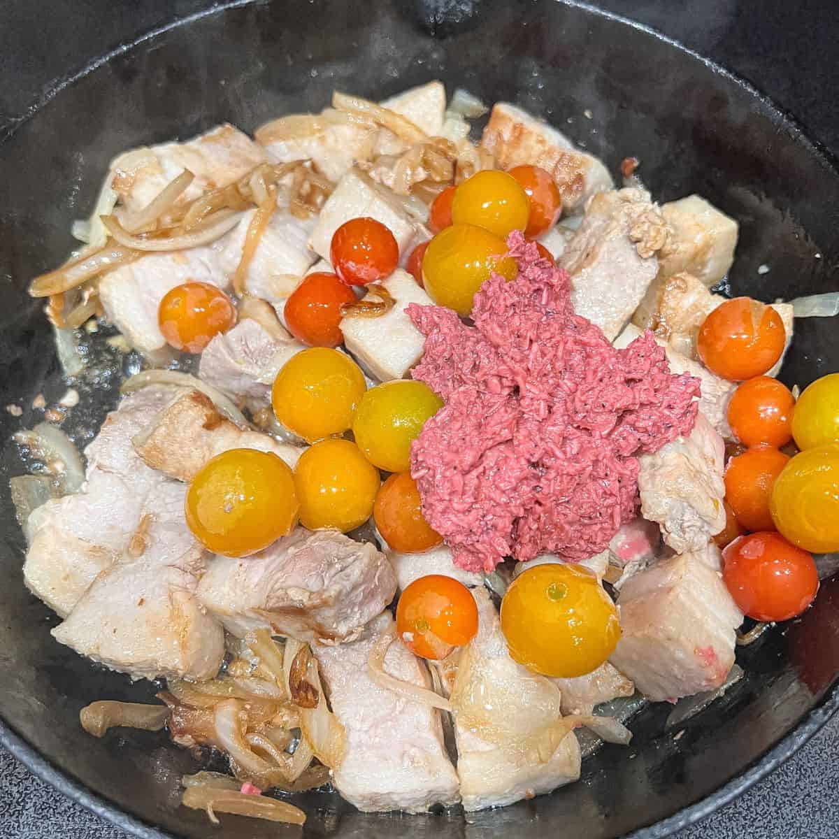 Adding tomatoes and shrimp paste to flavor and season the dish.